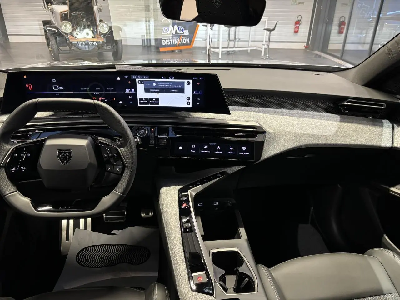 Vue intérieure avant de la Peugeot 3008 GT 2025, tableau de bord gris clair avec écran panoramique incurvé et volant compact noir.