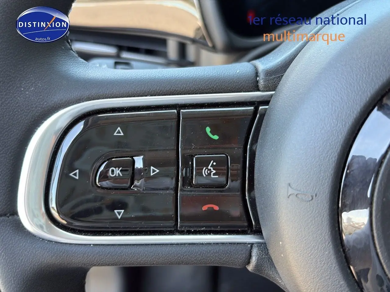 Gros plan sur les commandes multifonctions noires du volant de la FIAT 500 e blanche, version 2024.