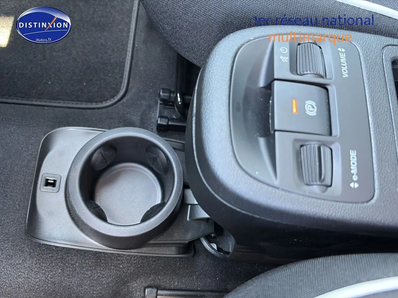 Gros plan sur la console centrale noire avec porte-gobelet et commandes volume et mode sur Fiat 500 électrique blanche.