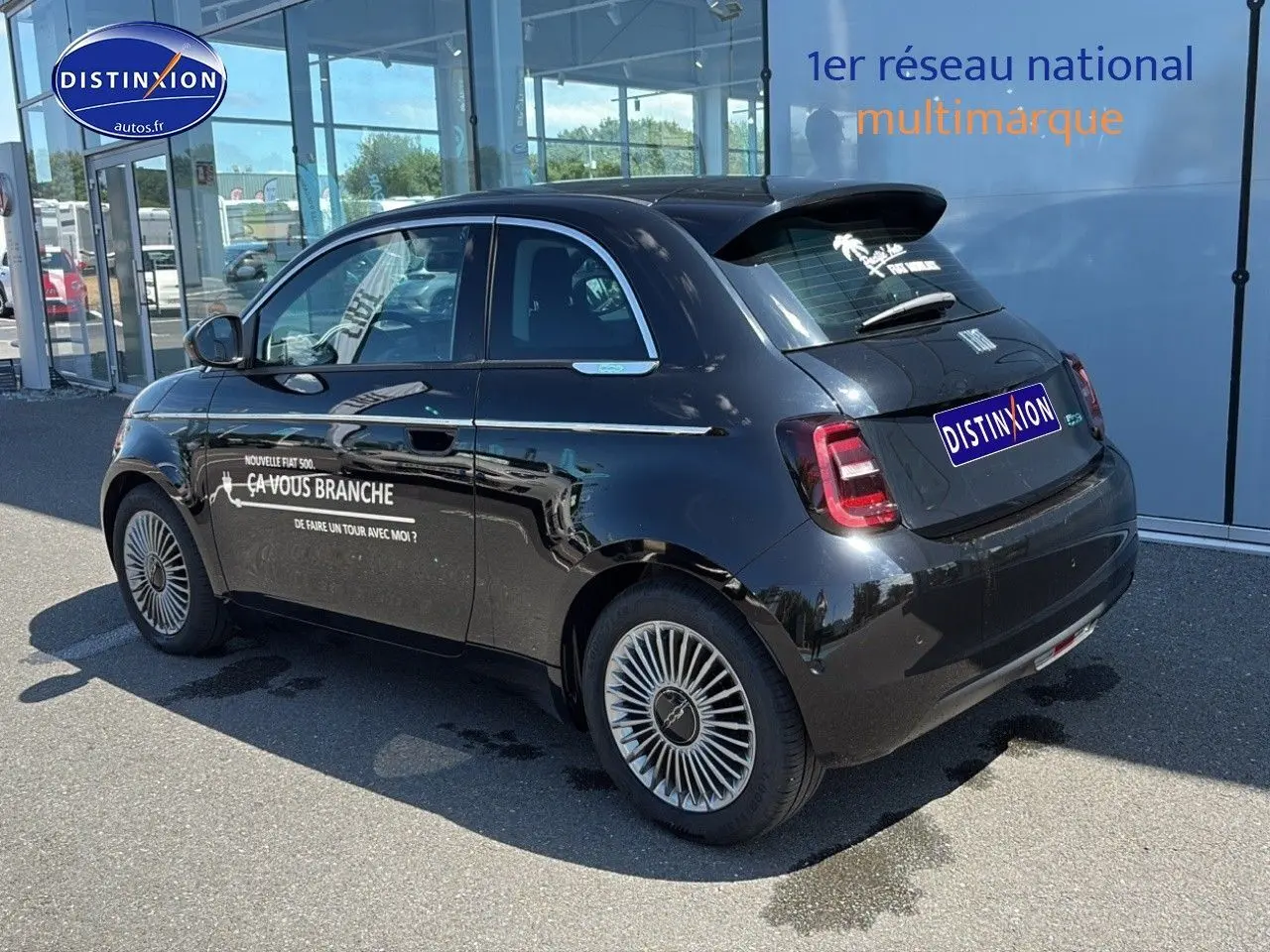 Vue 3/4 arrière droite d'une Fiat 500 électrique noire avec jantes alu et stickers publicitaires sur la porte.