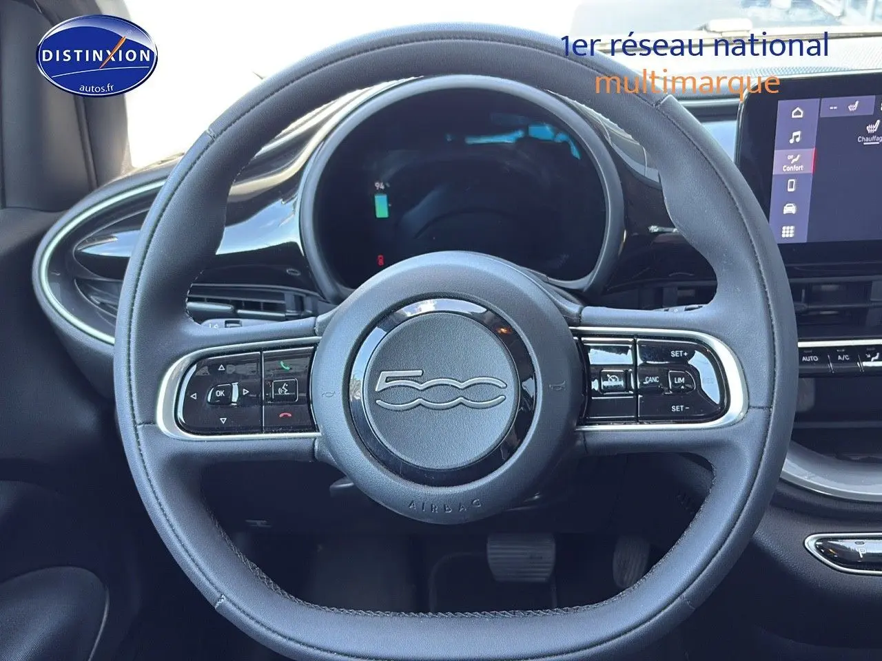 Vue rapprochée du volant multifonction noir de la FIAT 500 électrique blanche, avec tableau de bord numérique et écran tactile.