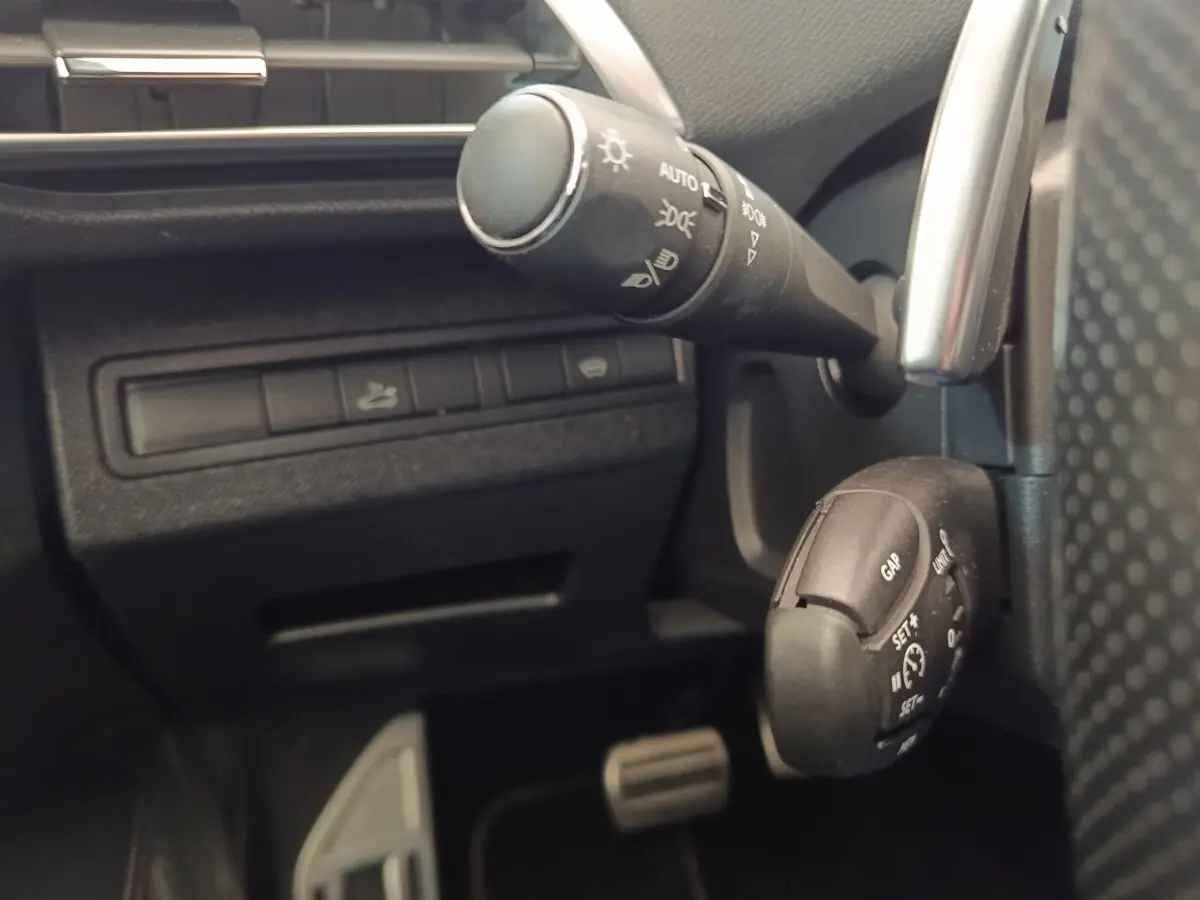 Détail intérieur du Peugeot 5008 gris clair 2019 montrant la commande des phares et le régulateur de vitesse au volant.