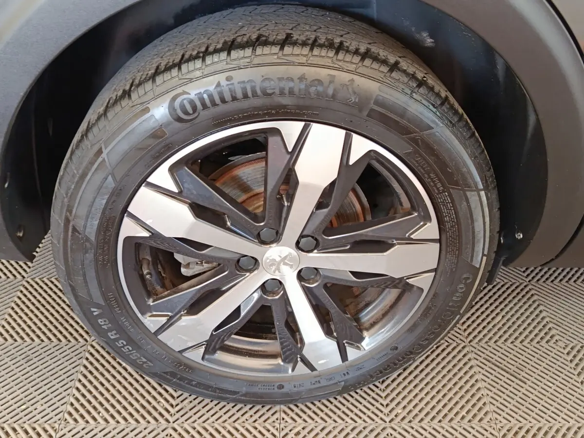 Gros plan sur la roue avant droite du Peugeot 5008 gris clair, mettant en valeur la jante alliage bicolore et le pneu Continental.