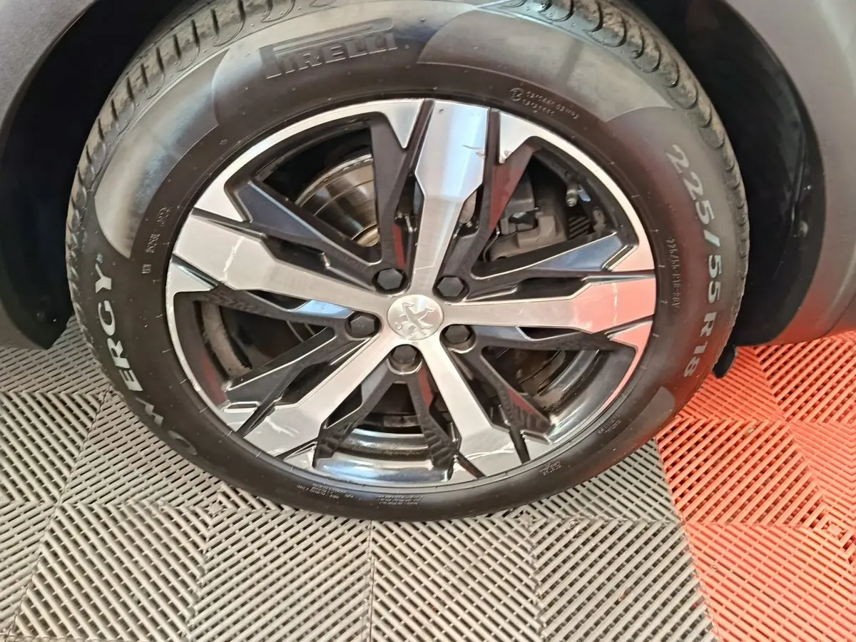 Gros plan sur la roue avant droite gris clair du Peugeot 5008 avec jante alliage noire et argentée, logo lion central visible.