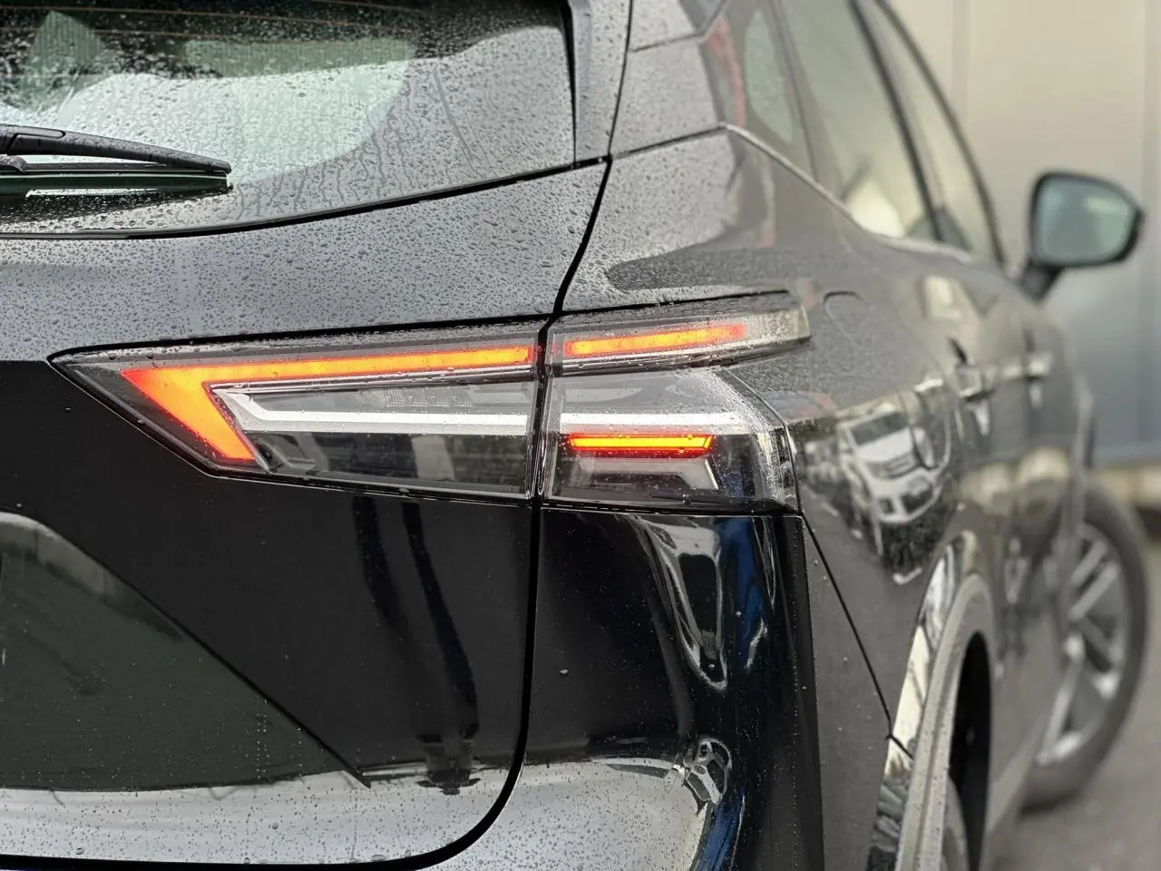Feu arrière droit allumé d’un Nissan Qashqai noir nacré vu en gros plan sous la pluie, avec reflet sur la carrosserie.