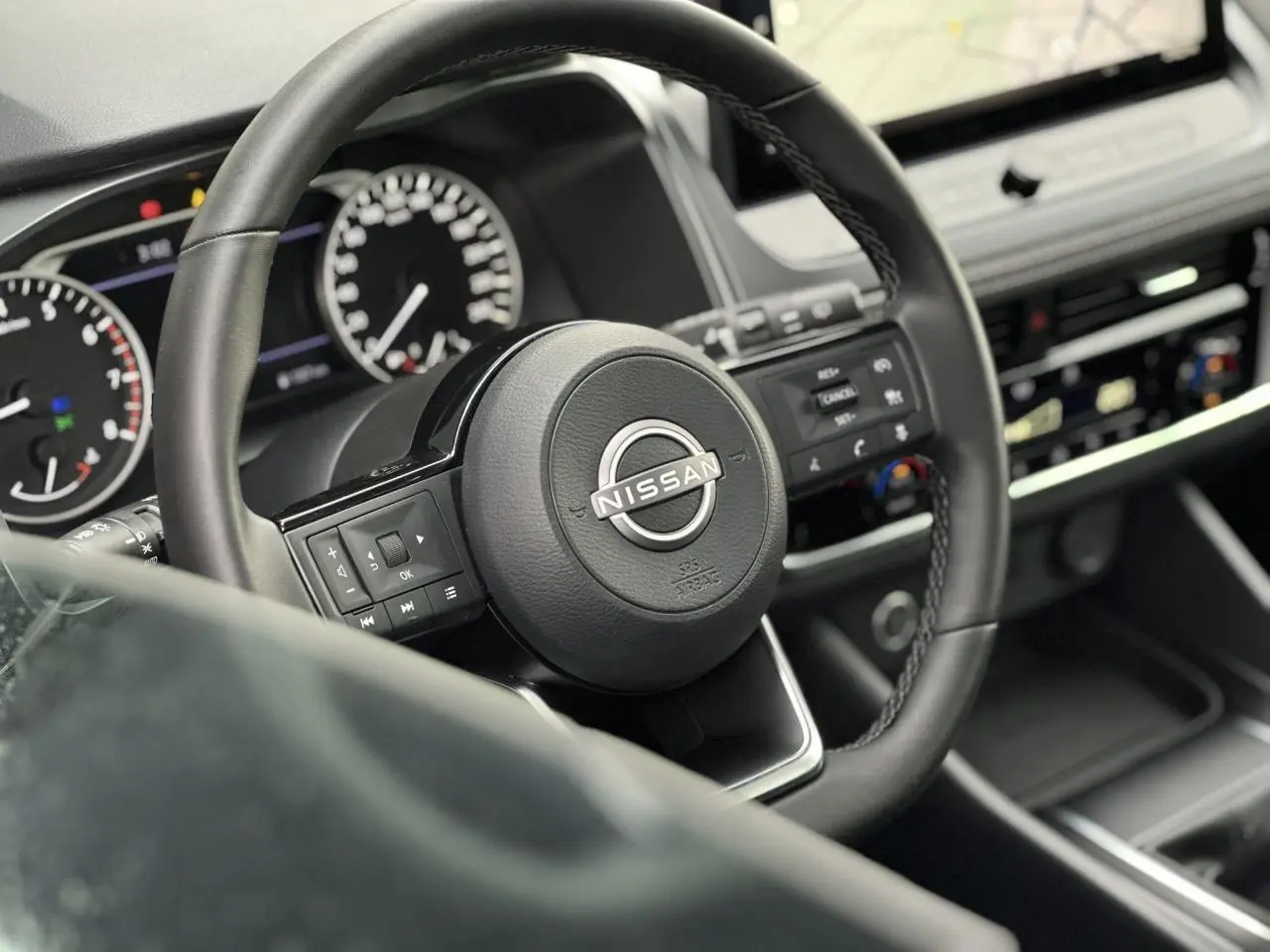 Vue rapprochée du volant noir du Nissan Qashqai 2025 avec commandes intégrées et tableau de bord digital flou.