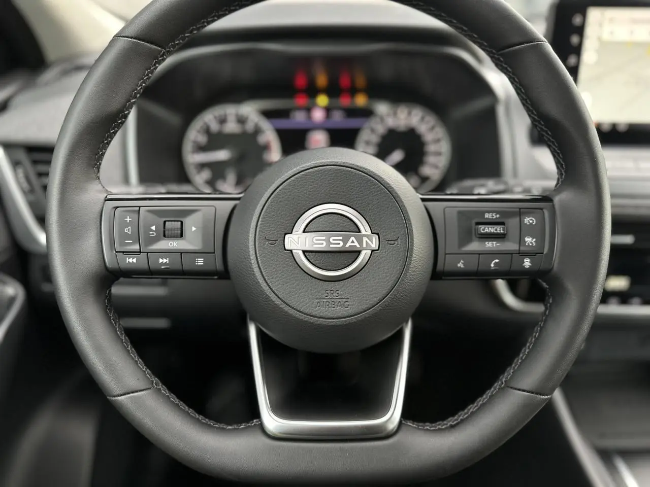 Gros plan sur le volant noir du Nissan Qashqai 2025 avec commandes intégrées et tableau de bord flou en arrière-plan.
