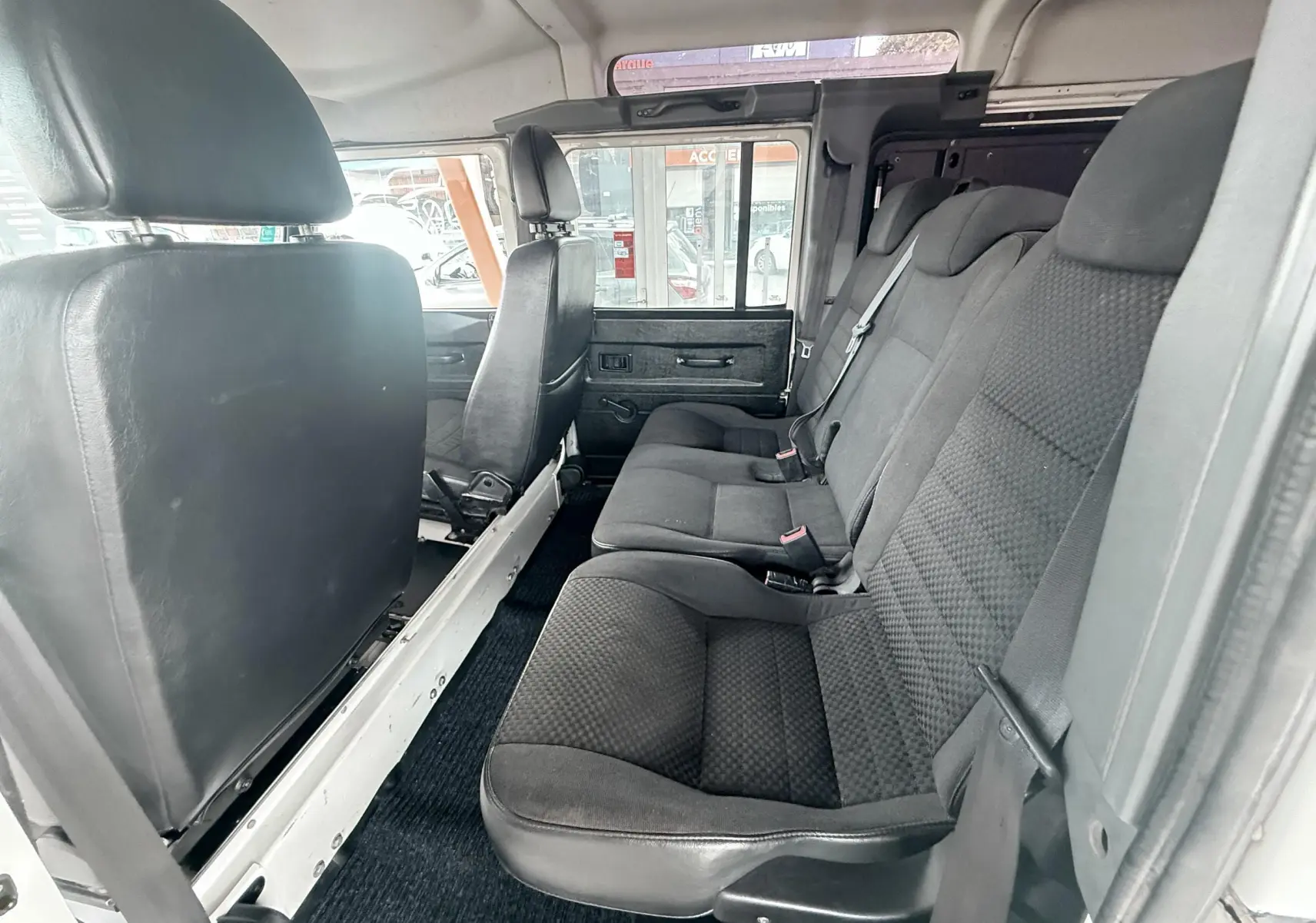 Vue intérieure côté droit du Land Rover Defender blanc 2007, montrant les sièges arrière en tissu gris noir et la porte ouverte.
