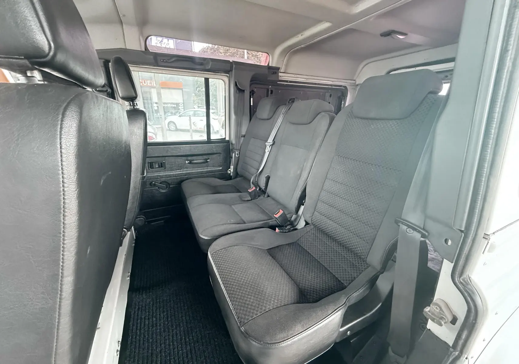 Vue intérieure côté droit des sièges arrière en tissu gris noir du Land Rover Defender blanc 5 portes de 2007.