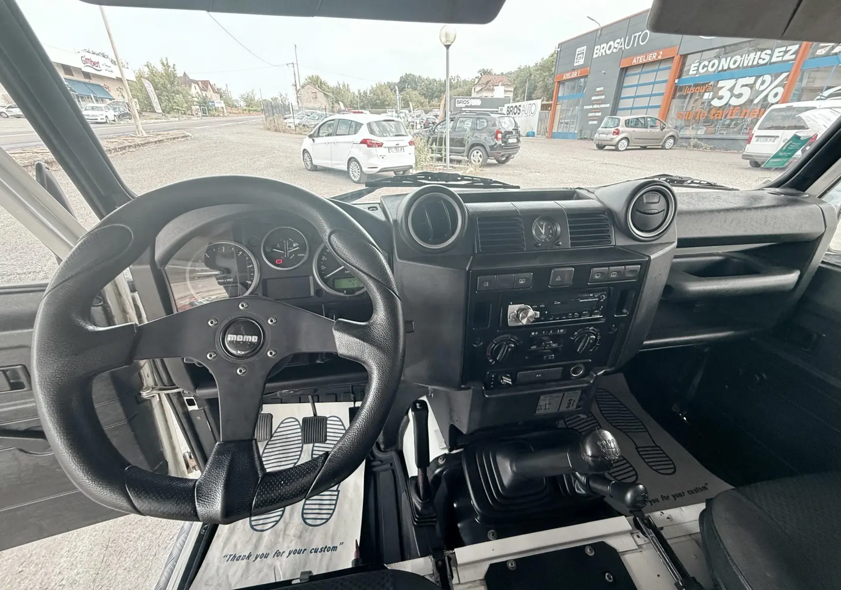 Vue intérieure du Land Rover Defender 2.4 TD4 2007, montrant le volant Momo, tableau de bord noir et levier de vitesses manuel.