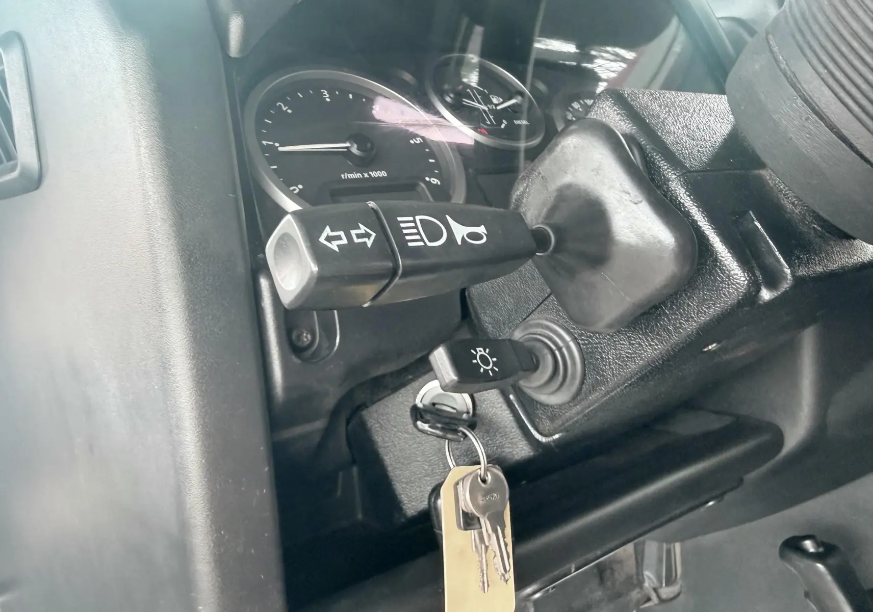 Gros plan sur la colonne de direction du Land Rover Defender blanc, montrant les commandes de clignotants et le contact avec clés.