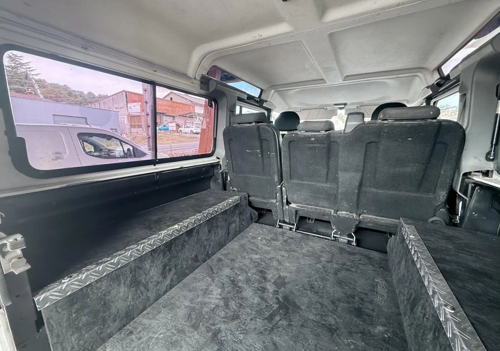 Vue intérieure arrière du Land Rover Defender blanc 2007, montrant les sièges arrière et l'espace de chargement aménagé.