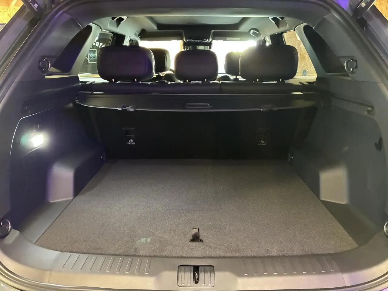 Coffre ouvert vu de l’arrière du JAECOO J7 gris olive, intérieur noir avec banquette arrière et éclairage.