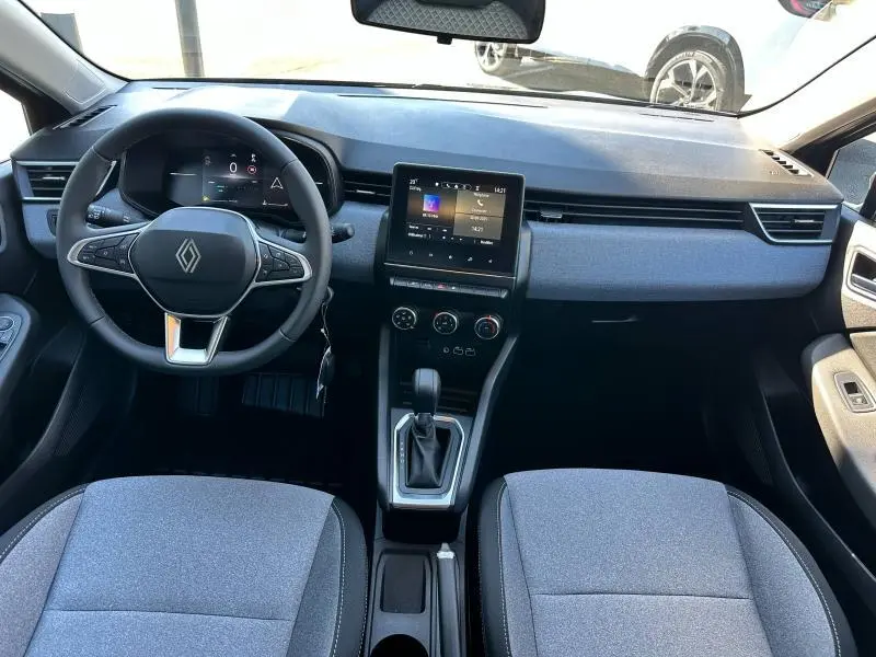Vue avant de l’habitacle gris de la Renault Clio 2025, volant multifonction, écran tactile central et sièges tissu gris.
