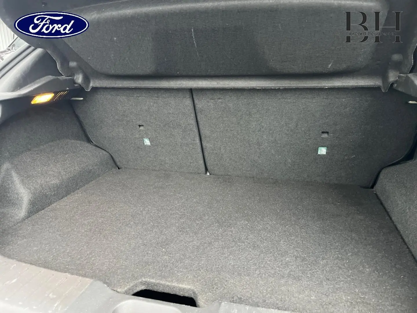 Coffre ouvert d'une Nissan Juke noir métallisé, vue intérieure montrant le tapis de sol et les parois en tissu gris.