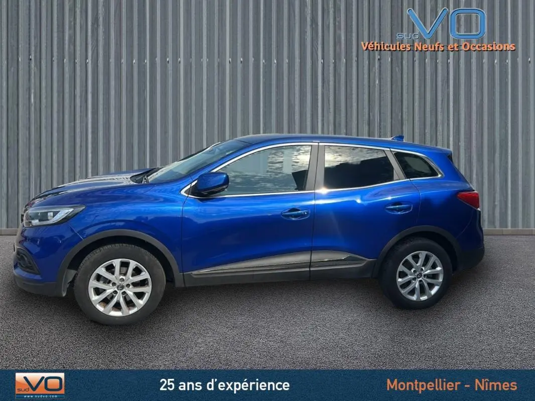Profil côté gauche d'un Renault Kadjar TCe 140 FAP Business bleu foncé avec jantes alliage et barres de toit visibles.