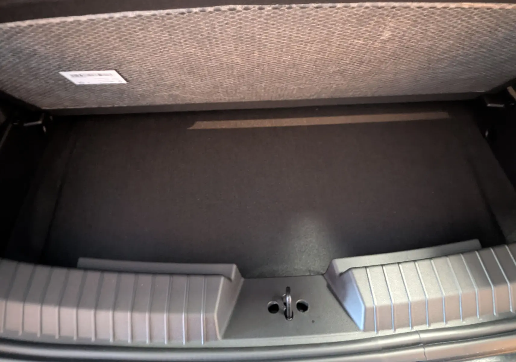 Vue plongeante sur le coffre noir du Dacia Duster 1.6 Hybrid 140ch Journey blanc glacier, montrant la surface de rangement.