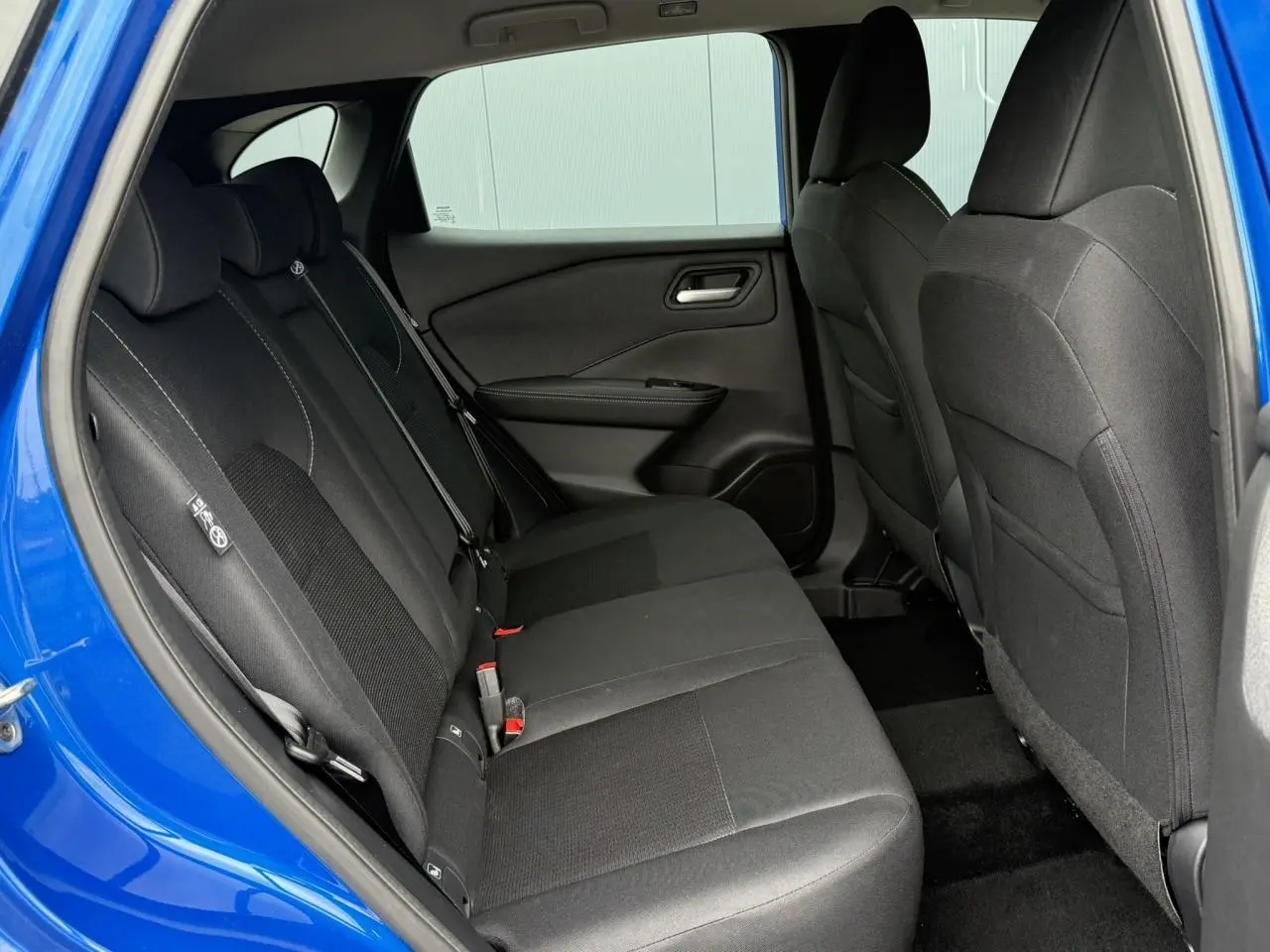 Vue intérieure côté gauche des sièges arrière noirs du Nissan Qashqai III bleu magnétique avec ceinture de sécurité visible.