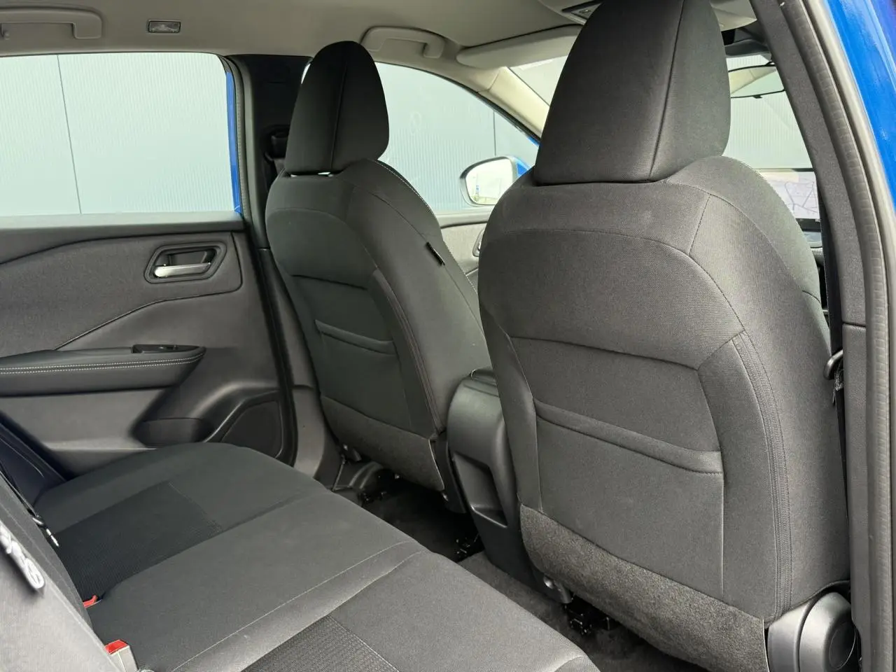 Vue intérieure arrière côté gauche du Nissan Qashqai bleu magnétique, montrant les sièges noirs en tissu.