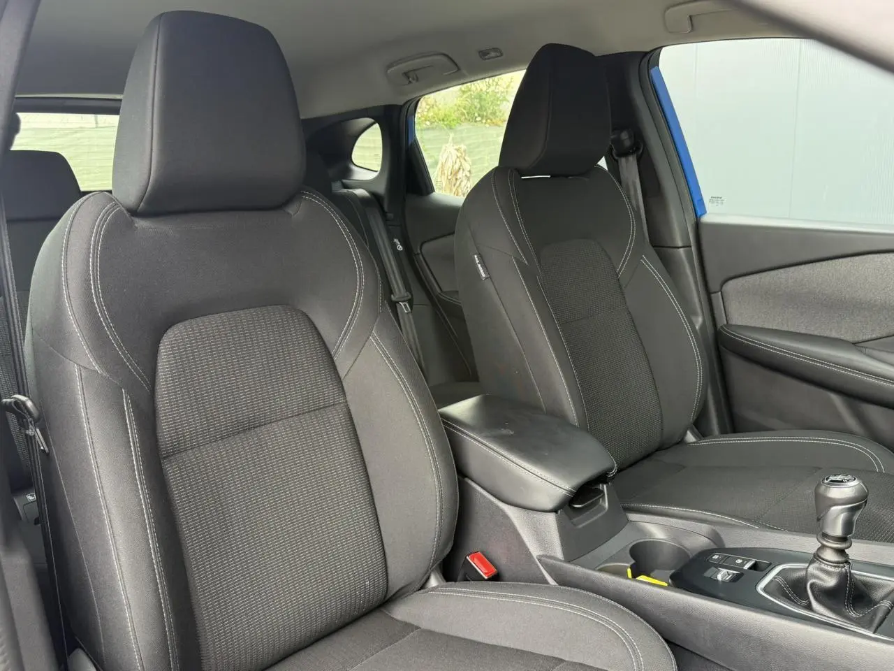 Vue intérieure côté avant droit du Nissan Qashqai 2025 bleu magnétique, montrant les sièges noirs et la console centrale.