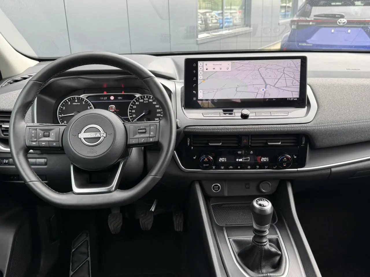 Vue intérieure du tableau de bord du Nissan Qashqai 2025, avec volant, écran tactile et levier de vitesses manuelle.