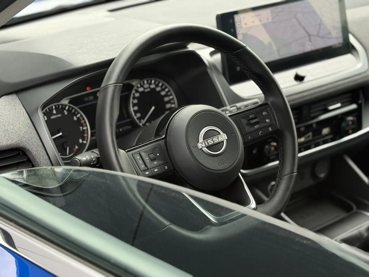 Vue intérieure rapprochée du volant noir Nissan Qashqai 2025 avec tableau de bord et écran tactile visible.