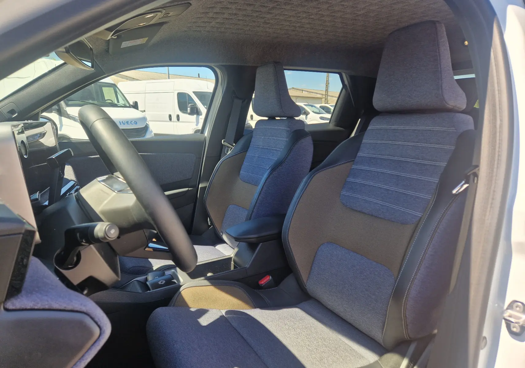 Vue intérieure côté conducteur de la Renault R5 E-TECH 2025, sièges tissu bleu et gris avec accoudoir central.