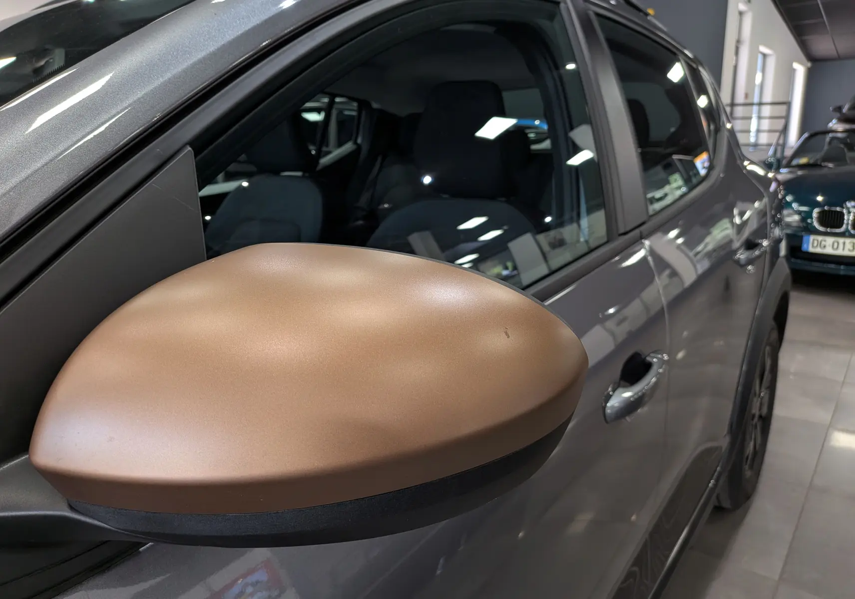 Gros plan sur le rétroviseur droit bronze du Dacia Sandero Stepway gris schiste, vue latérale en intérieur showroom.