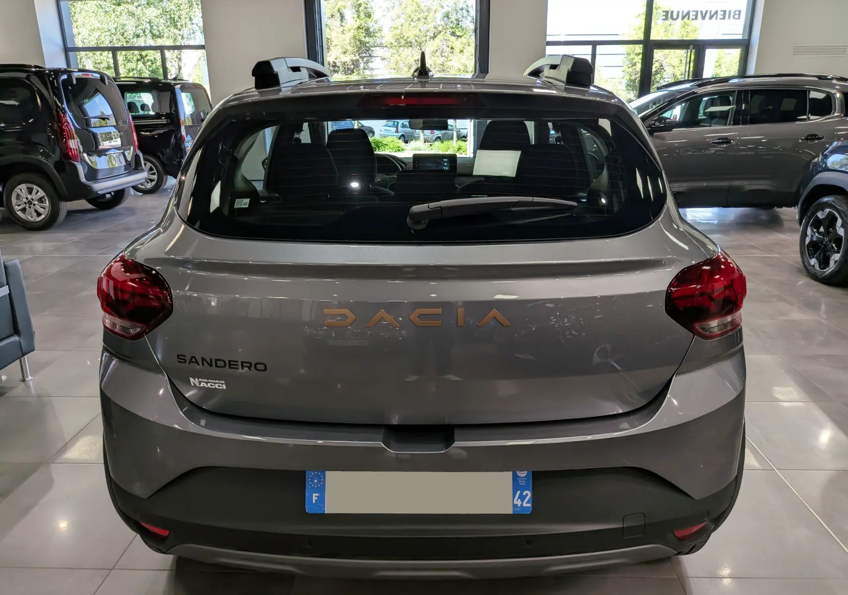 Vue arrière d'une Dacia Sandero Stepway gris schiste en showroom, avec logo Dacia et feux arrière rouges visibles.