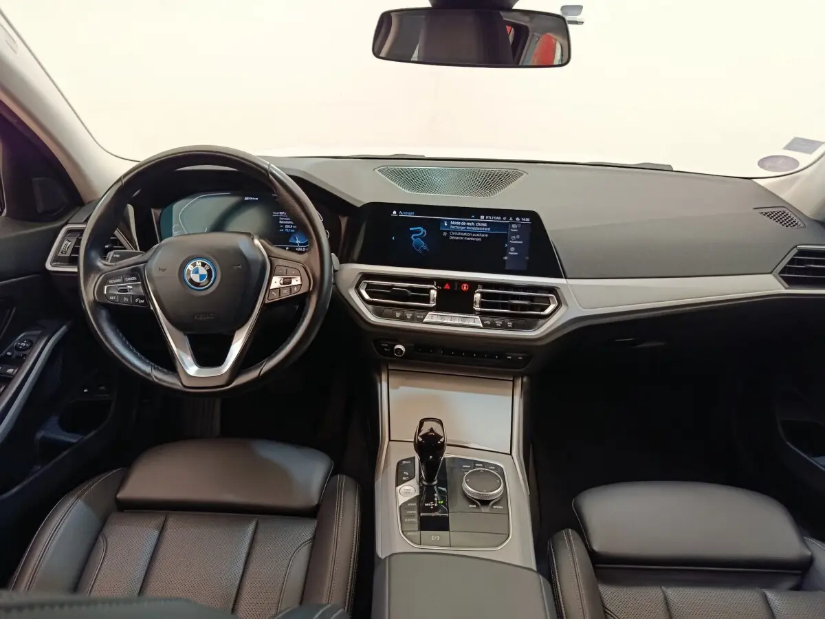 Vue intérieure avant de la BMW Série 3 320e hybride, tableau de bord noir avec écran tactile et volant cuir multifonctions.