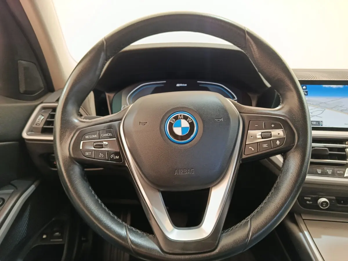 Vue rapprochée du volant cuir noir de la BMW Série 3 320e hybride avec tableau de bord numérique et écran tactile.