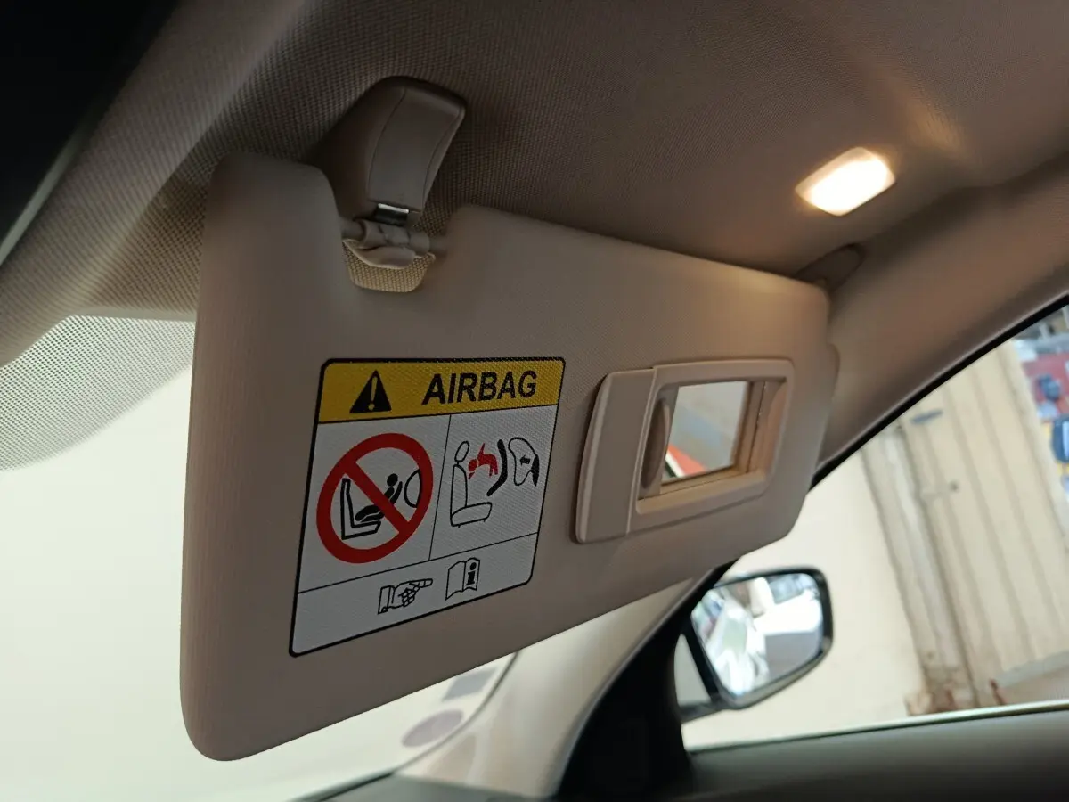 Détail du pare-soleil côté conducteur beige avec avertissement airbag dans une BMW Série 3 blanche hybride.