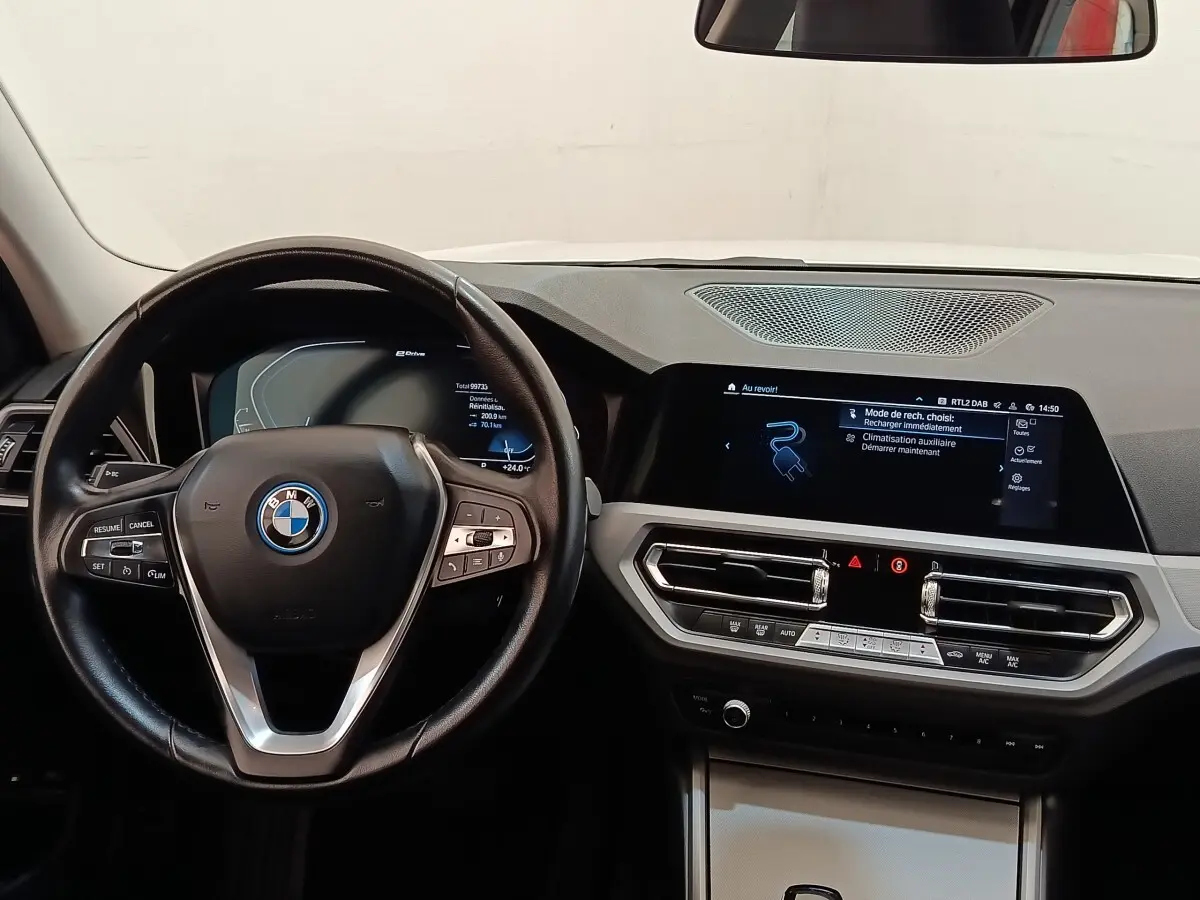 Vue intérieure frontale du tableau de bord et volant noir de la BMW Série 3 320e hybride, avec écran tactile et commandes intégrées.
