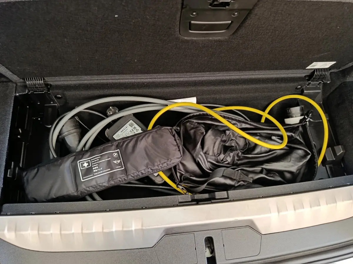 Coffre ouvert d’une BMW Série 3 hybride blanche, vue plongeante sur câbles de recharge et accessoires rangés.