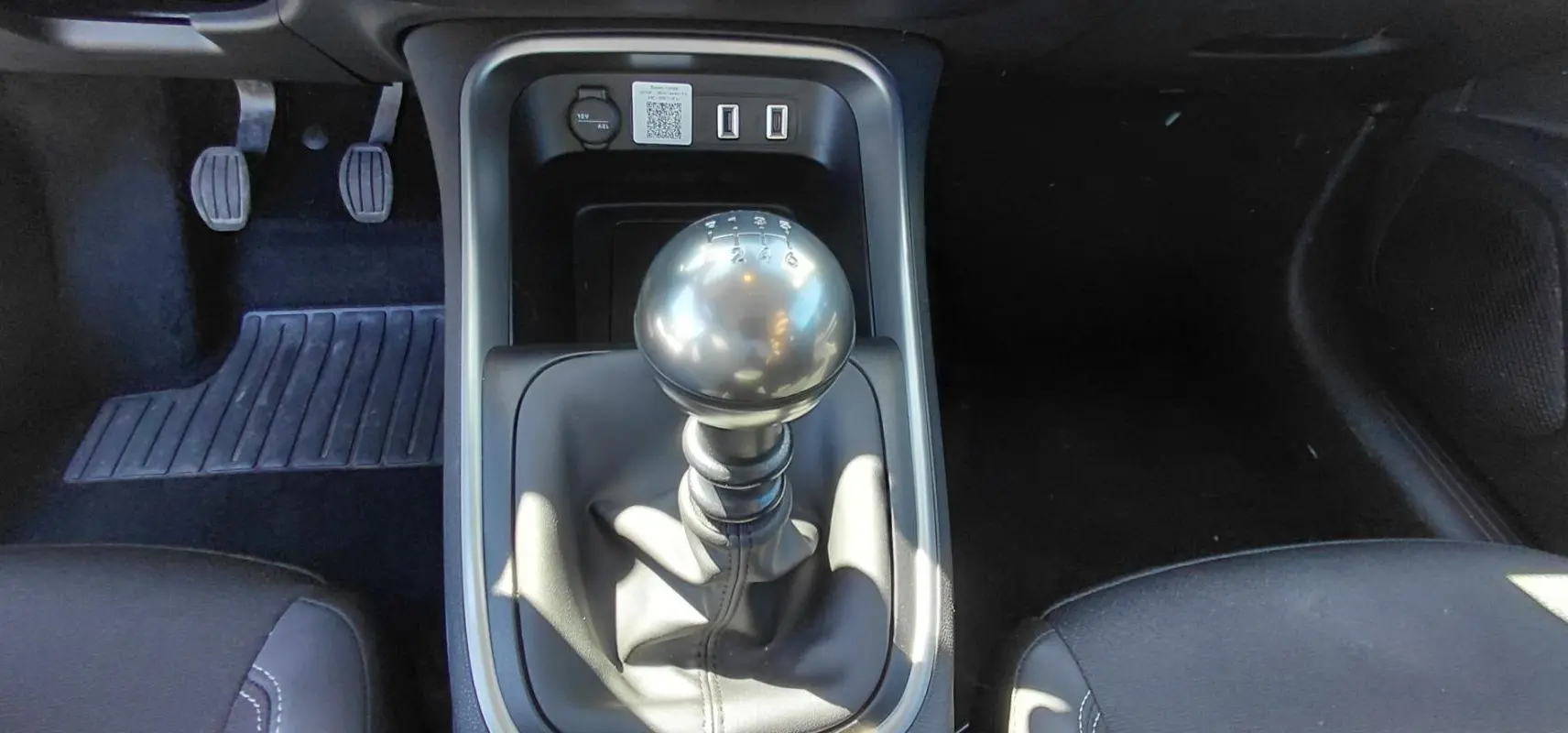 Le levier de vitesses manuel noir du Jeep Avenger blanc 2025, vu de dessus avec pédales et sièges partiels.