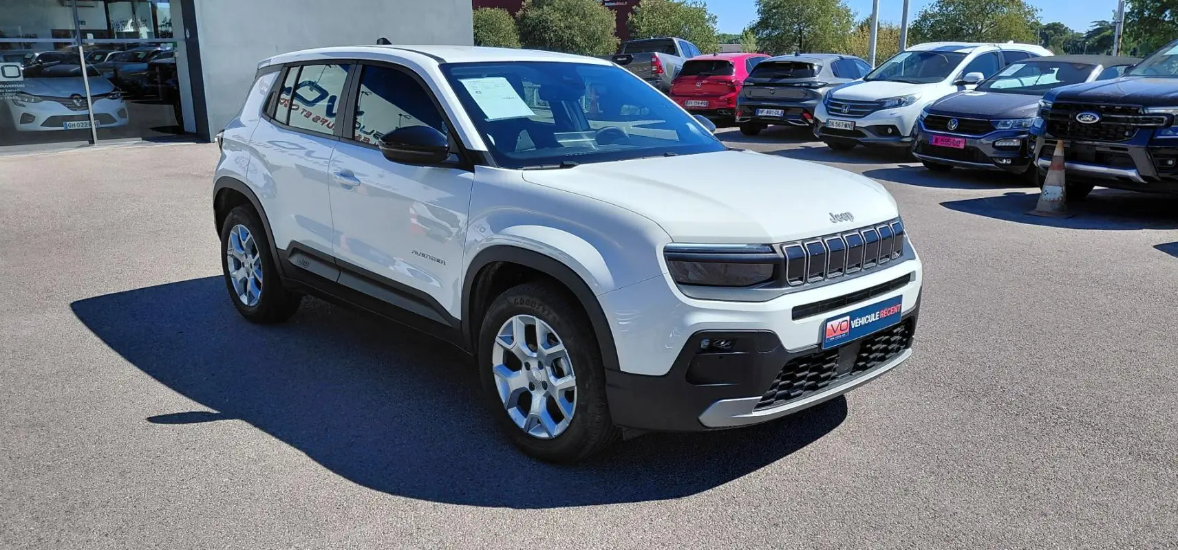 Jeep Avenger blanc en 3/4 avant droit, avec calandre distinctive et jantes alu, stationné en extérieur.