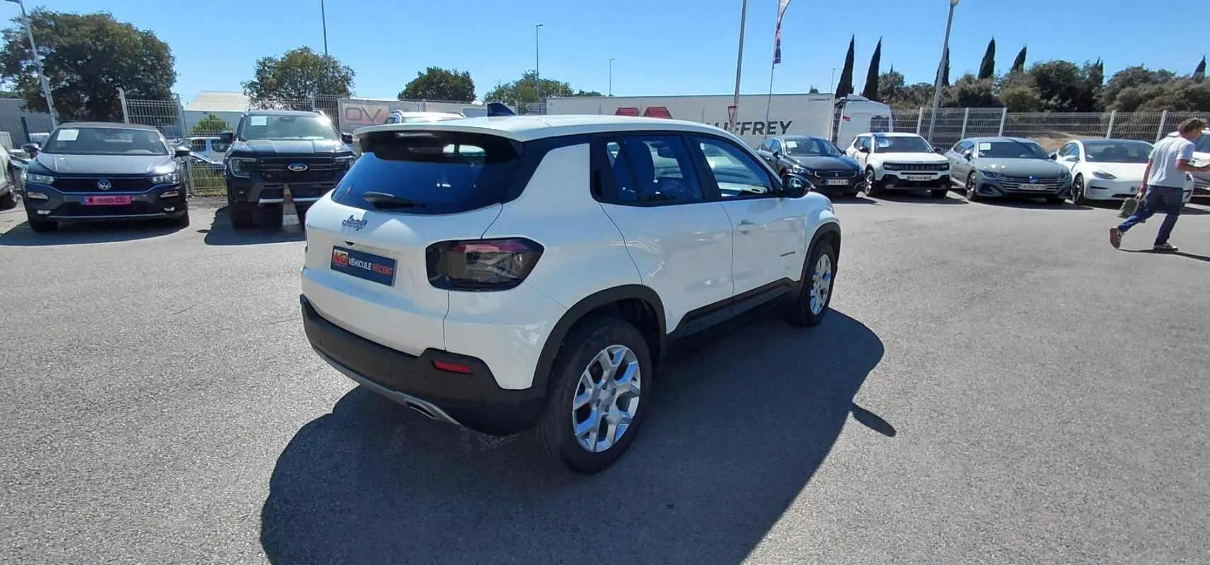 Jeep Avenger blanc vu en 3/4 arrière droit, avec feux arrière fumés et jantes alliage, stationné en extérieur.