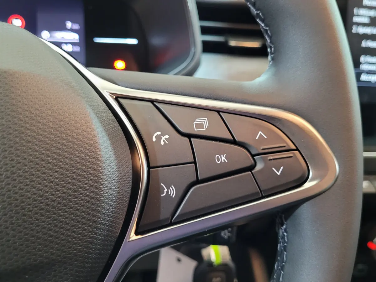Gros plan sur les commandes multifonctions à droite du volant cuir d'une Renault Clio bleu 2025.