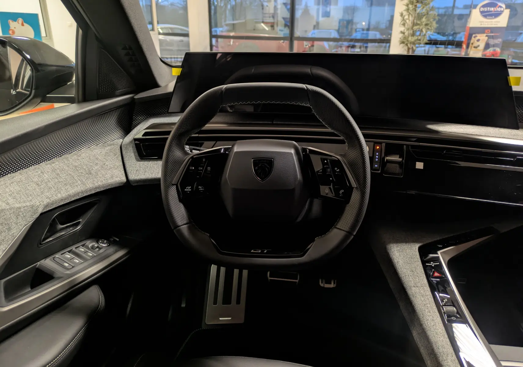 Vue intérieure centrée sur le volant compact noir du Peugeot 3008 Hybrid 2025 avec tableau de bord numérique et pédalier alu.