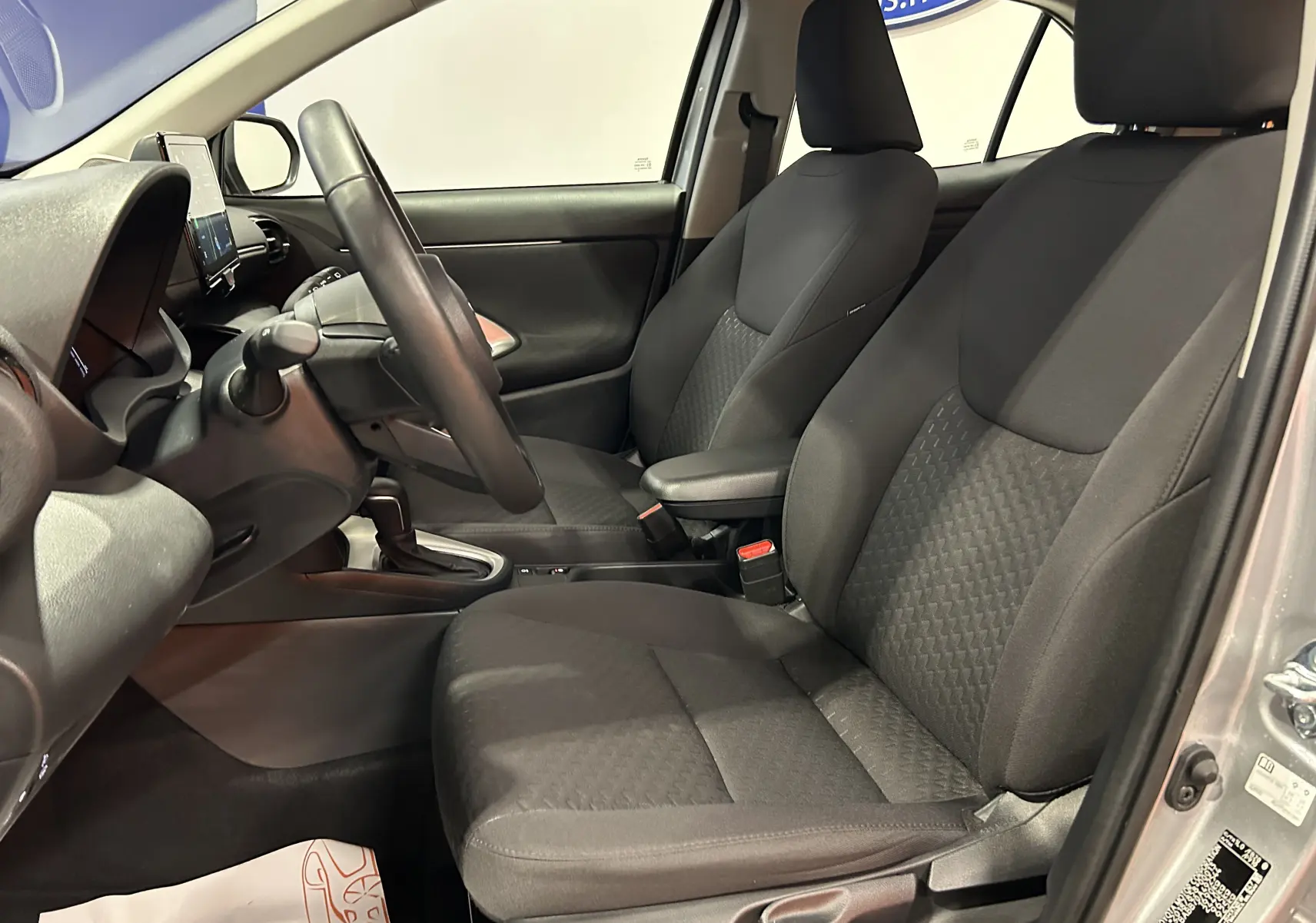 Vue intérieure côté conducteur de la Toyota Yaris Cross gris minéral, montrant les sièges en tissu et le volant noir.