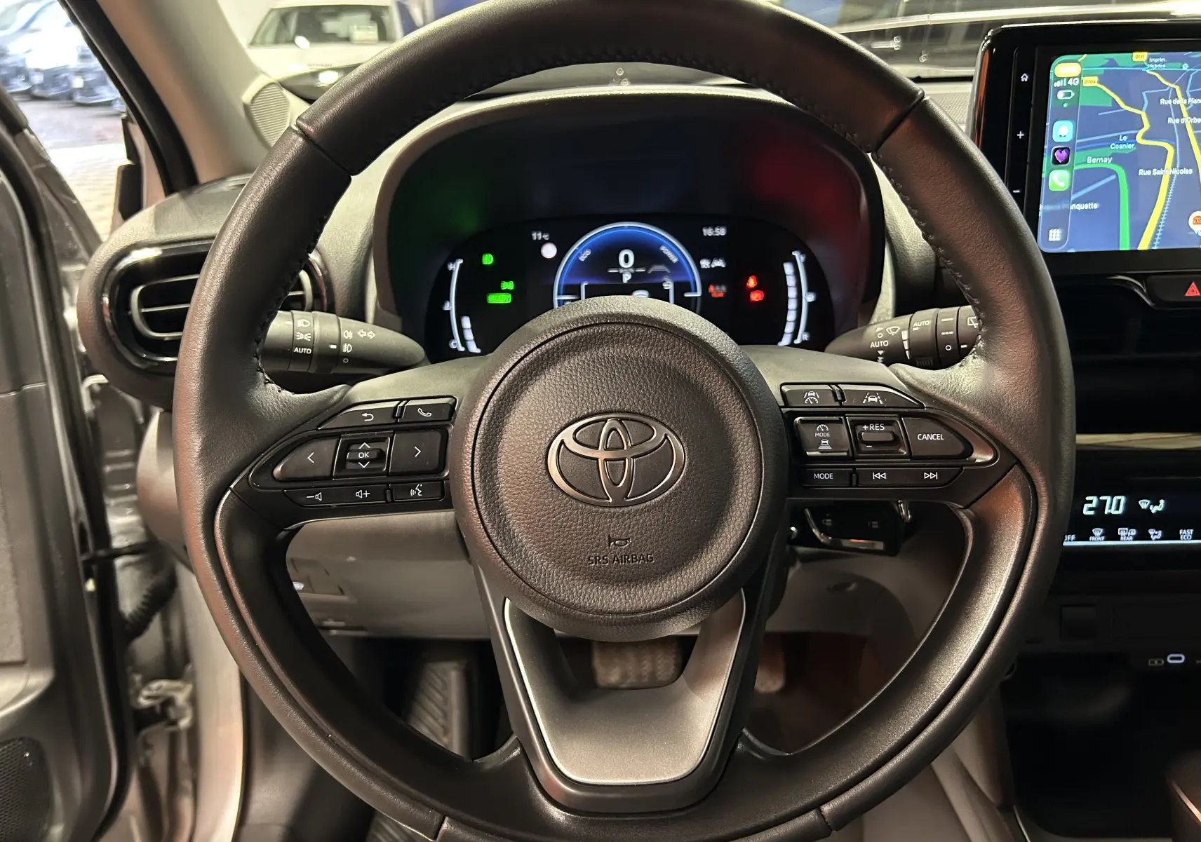 Vue centrée sur le volant cuir noir de la Toyota Yaris Cross 2025, avec tableau de bord digital et écran tactile GPS visible.