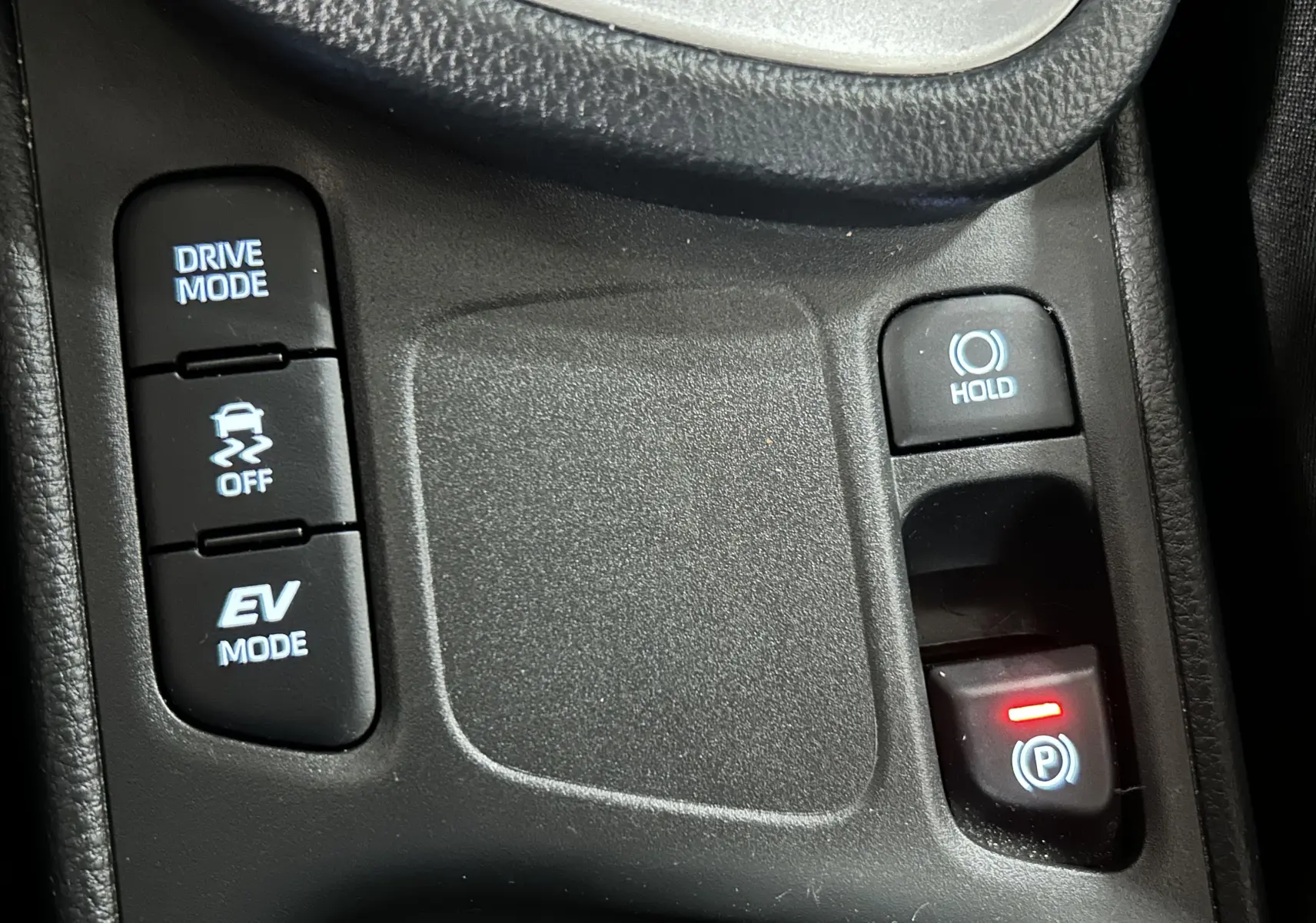 Gros plan sur les boutons de commande du mode de conduite et frein à main électronique dans une Toyota Yaris Cross gris minéral.