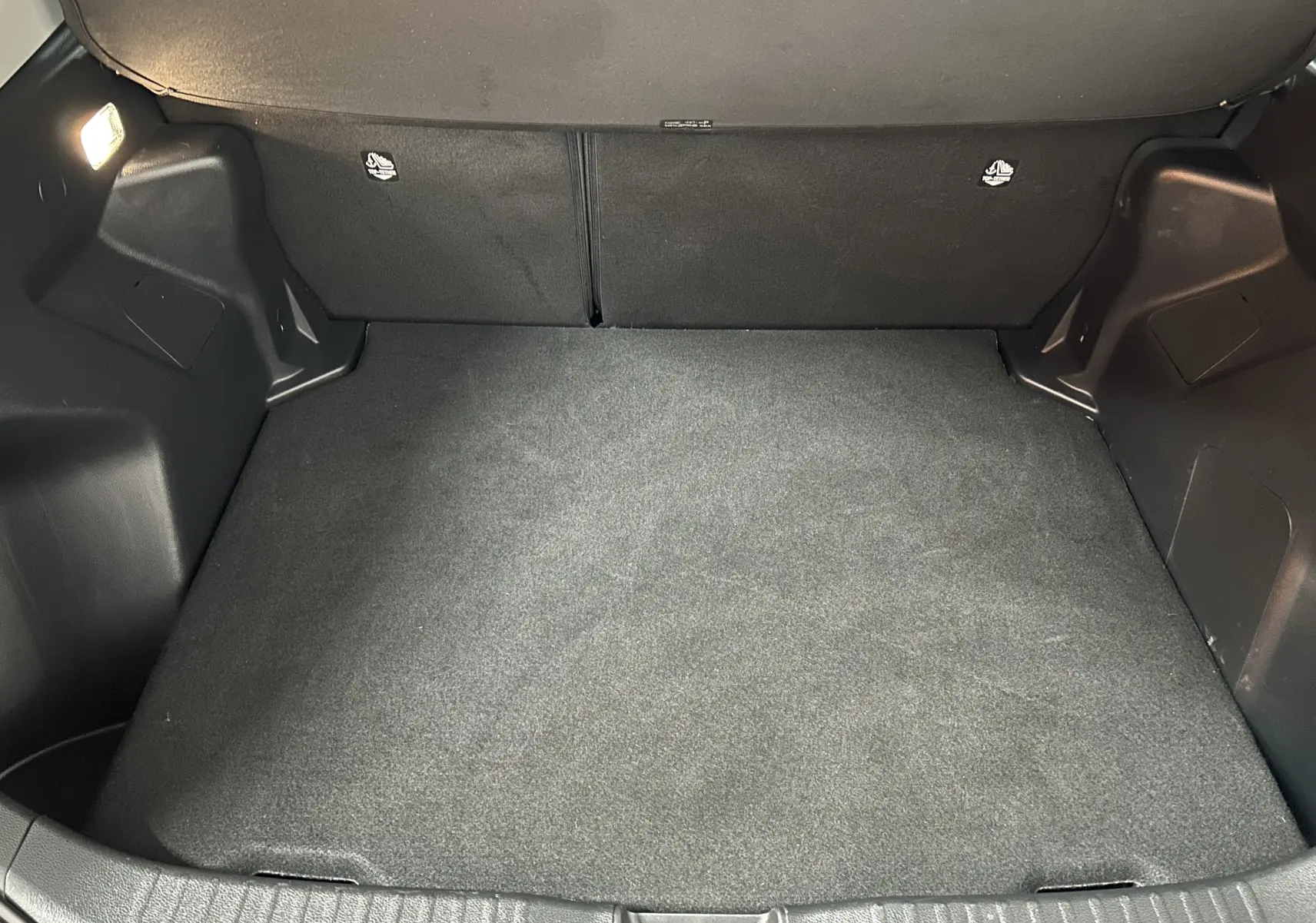 Vue intérieure du coffre spacieux et propre de la Toyota Yaris Cross 116h Active gris minéral, avec éclairage latéral allumé.