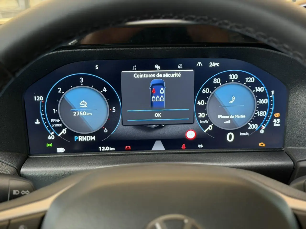 Vue rapprochée du tableau de bord numérique du Volkswagen Transporter T7 gris Stone, affichant les compteurs et alertes de sécurité.