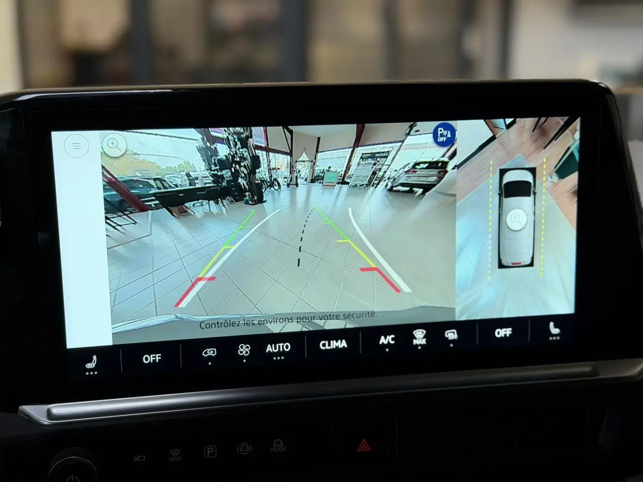 Écran tactile montrant la caméra de recul et vue 360° du Volkswagen Transporter gris Stone en intérieur showroom.