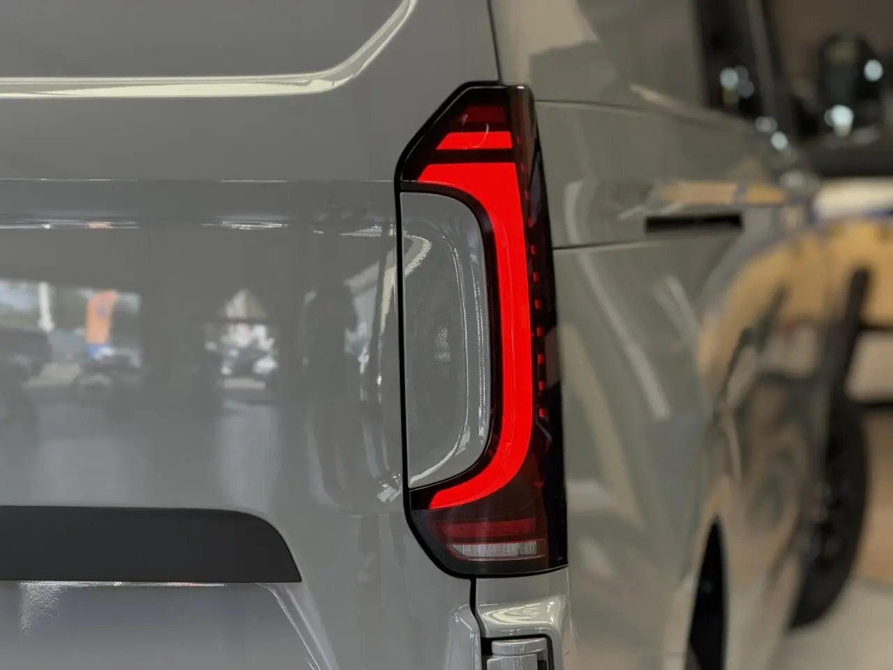 Gros plan sur le feu arrière LED rouge du Volkswagen Transporter T7 ProCab gris Stone, côté gauche arrière.