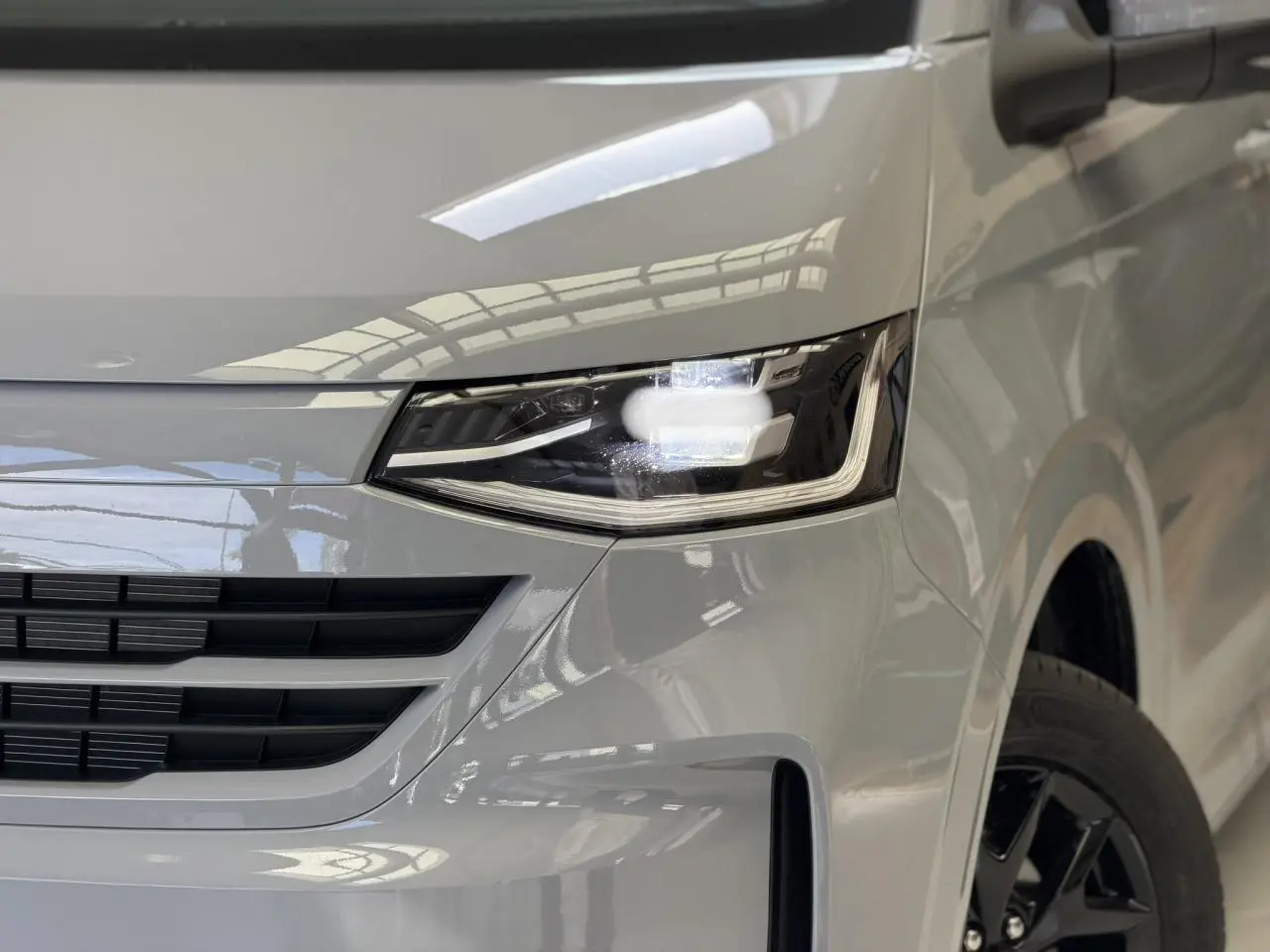 Gros plan sur l'avant droit du Volkswagen Transporter T7 gris Stone, avec phare LED Matrix et jante alliage noir brillant.