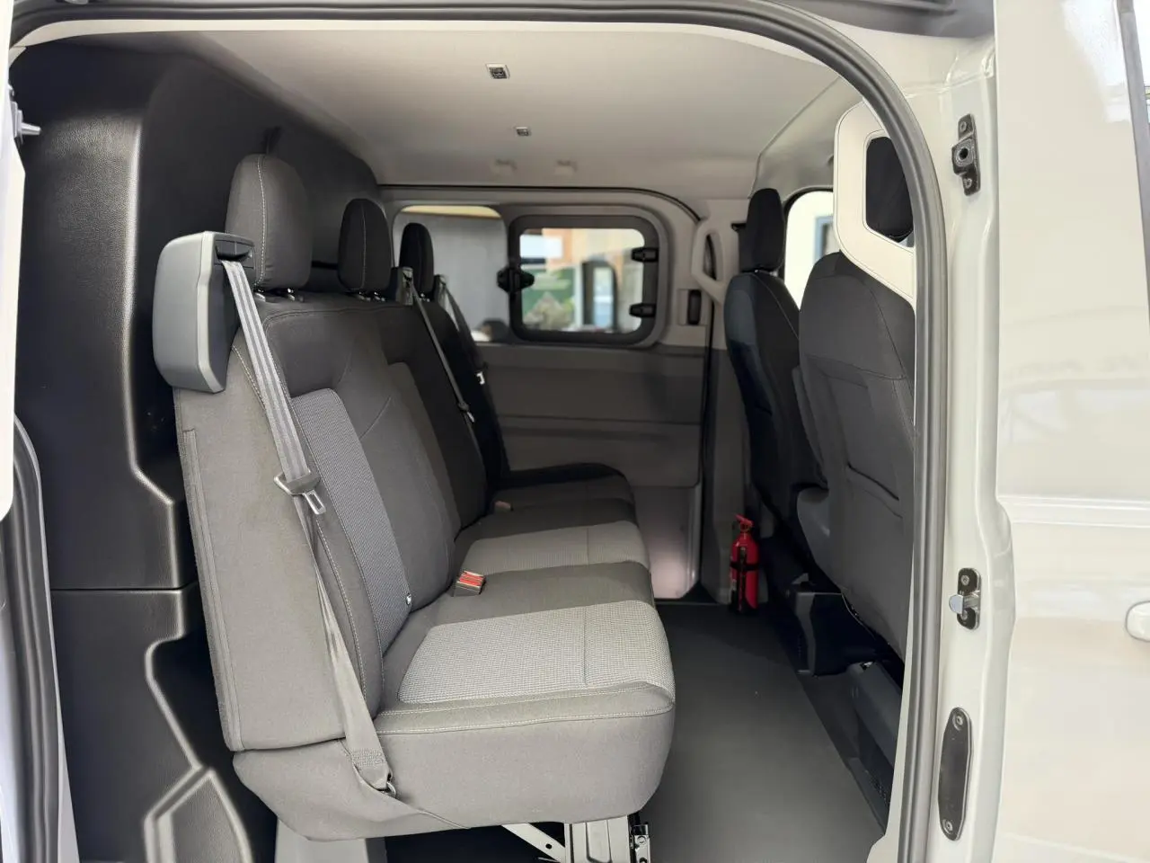 Vue latérale intérieure du Volkswagen Transporter T7 ProCab gris Stone, montrant les sièges arrière en tissu à rayures.