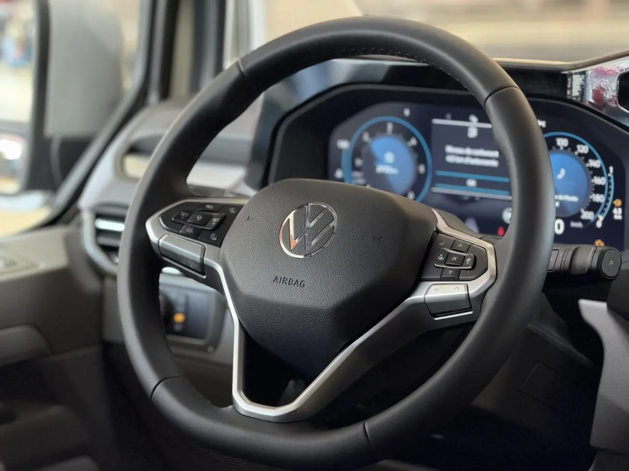 Vue rapprochée du volant multifonction noir du Volkswagen Transporter T7 avec tableau de bord digital en arrière-plan.