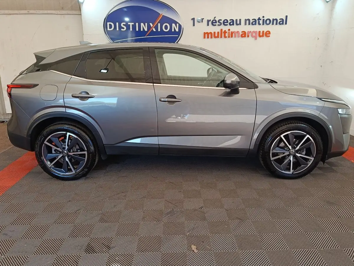 Vue de profil côté gauche d'un Nissan Qashqai gris foncé avec jantes alliage et toit noir en intérieur showroom.